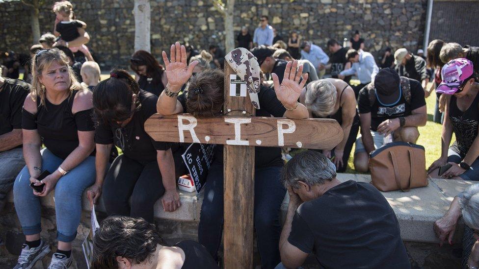 A white protester leans on a cross while others kneel on the ground to protest farm murders in South Africa.