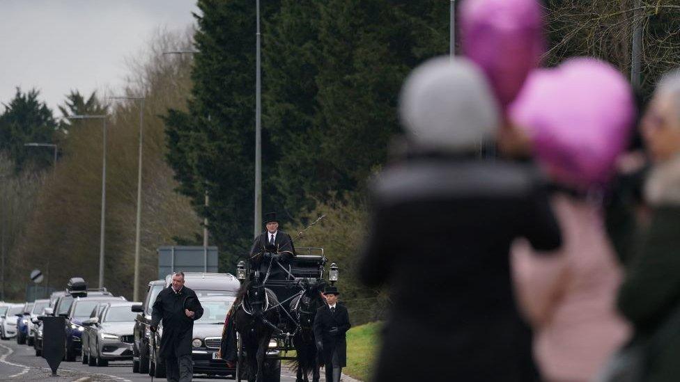 Mourners hold pink balloons on the street as they wait for Ms Croucher's funeral cortege to pass