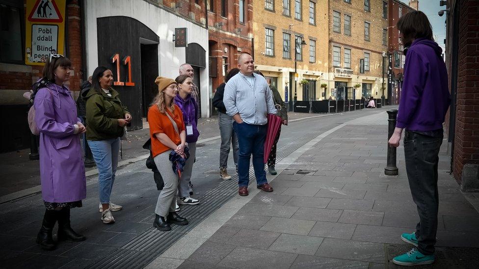 Johnny Giles standing on Womanby Street in Cardiff speaking to a group of about a dozen people taking the tour