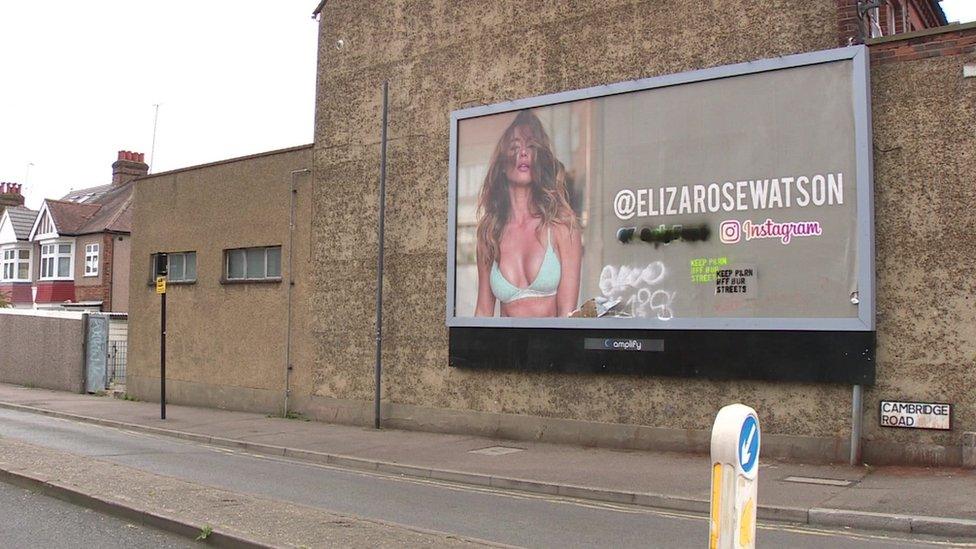 The billboard advert in Harrow, showing Eliza with hair over her face and wearing a green plunge bra.