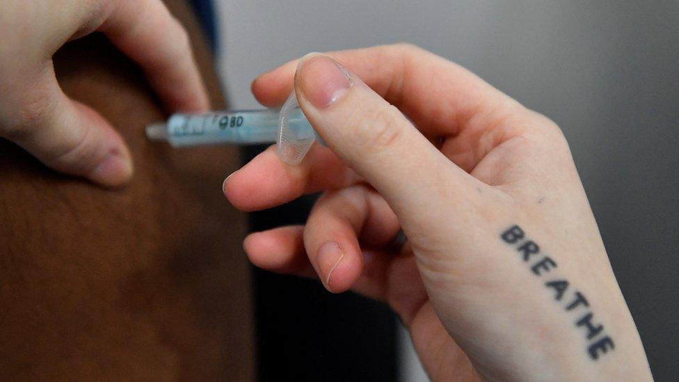 A Covid-19 booster vaccine injected into an arm by someone with the word breathe tattooed on their hand