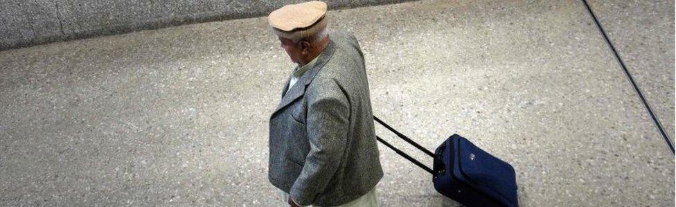 An older man wearing clothing indicating he may be a Muslim wheels a suitcase through the international arrivals hall at Washington Dulles International Airport in Virginia (February 2017)