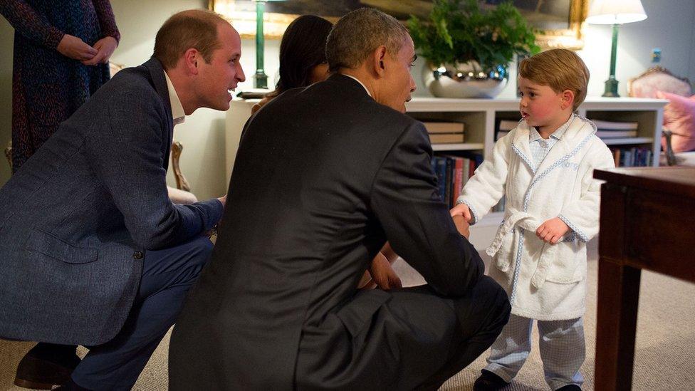 Britain's Prince George shakes hands with a kneeling Barack Obama, while the first lady and George's father, Prince William, look on.