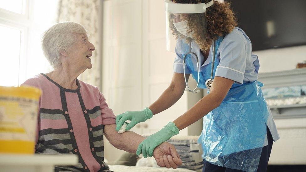 A carer helps an older woman get dressed in her bedroom