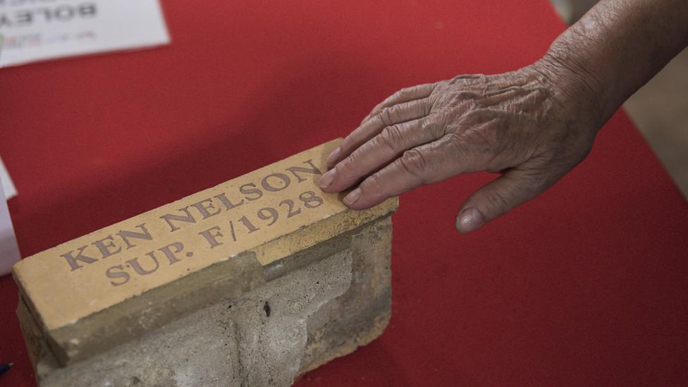 Hand touching brick labelled Ken Nelson