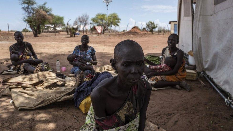 A cholera-stricken woman showing signs of malnutrition sits next to fellow patients (background) outside a temporary field hospital near the remote village of Dor in the Awerial county in south-central Sudan on April 28, 2017