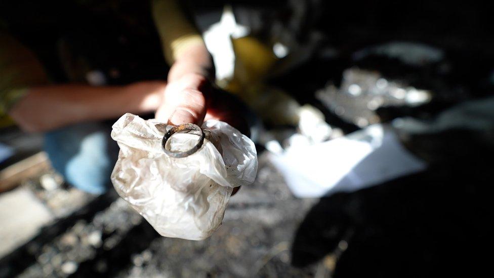 A hand holds what looks like a rusted and charred wedding ring