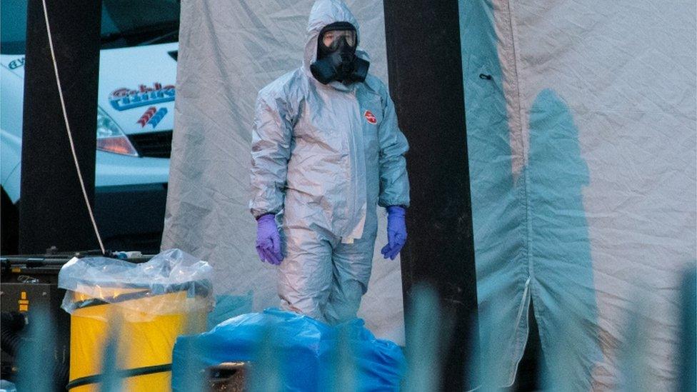 A police officer in a forensics suit and protective mask stands by a forensics tent in Salisbury