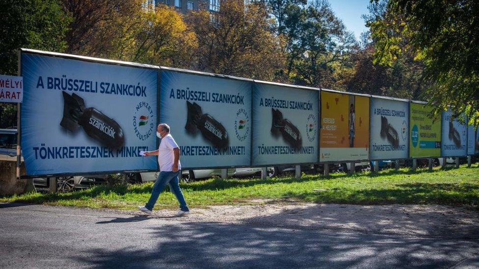 A man passes by posters depicting a bomb reading "We are being punished by the Brussels sanctions", in Budapest on October 18, 2022