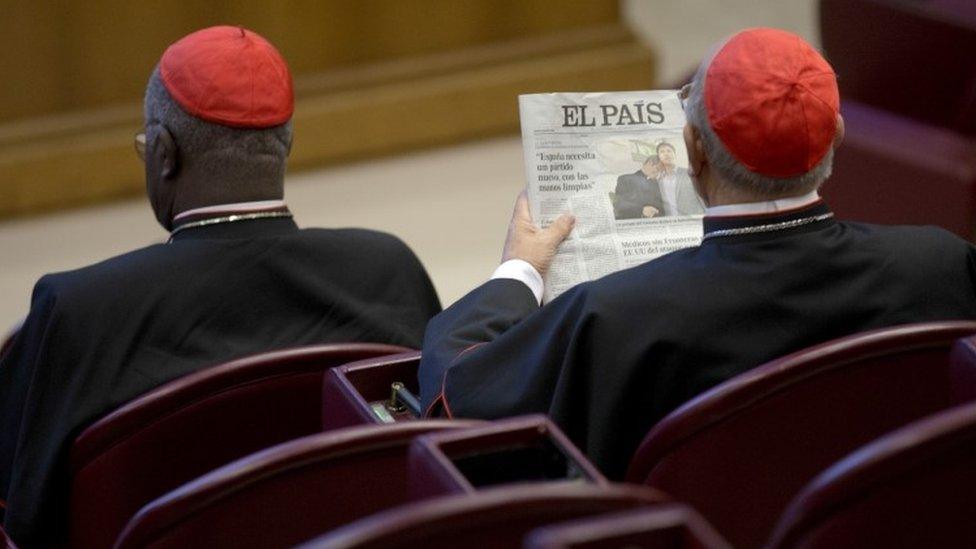 A cardinal attending the Synod on the Family reads a newspaper showing a picture of gay bishop Krzysztof Charamsa and his partner Eduard before the start of the morning session (09 October 2015)