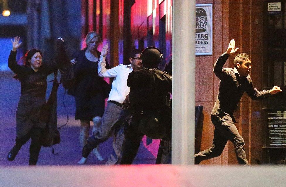 People run with there hands up from the Lindt Cafe, Martin Place during a hostage standoff on December 16, 2014 in Sydney