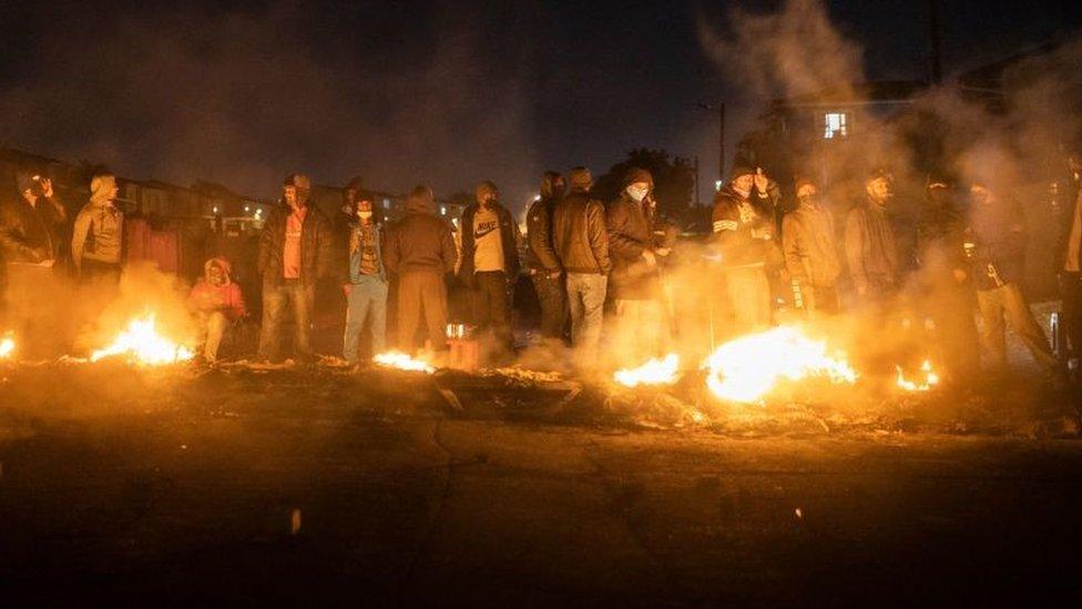 Armed community members gather around a fire to keep warm at a road block set up in Phoenix Township, North Durban, on July 15, 2021 to prevent looters from reaching the community