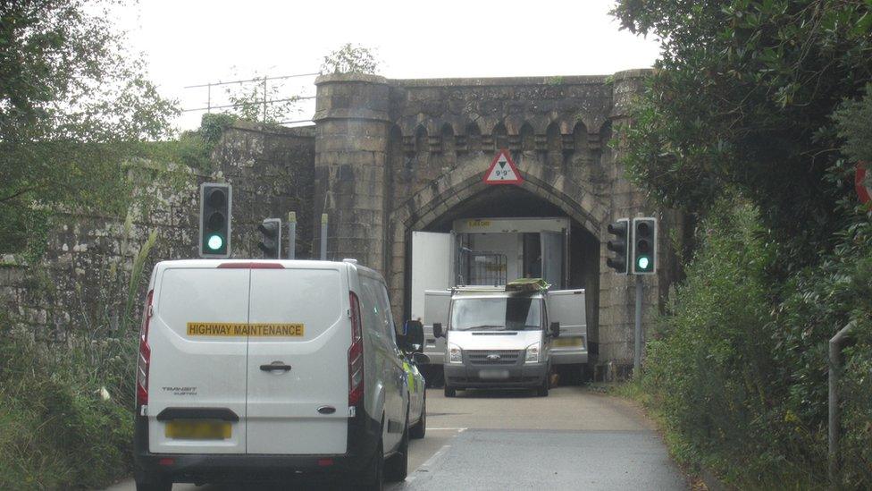 Highway maintenance and police car attend the scene where a lorry is stuck under a bridge