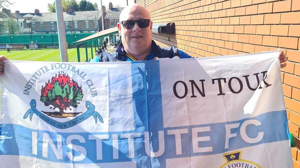 Geoff Graham holds a white and blue flag bearing the Institute crest