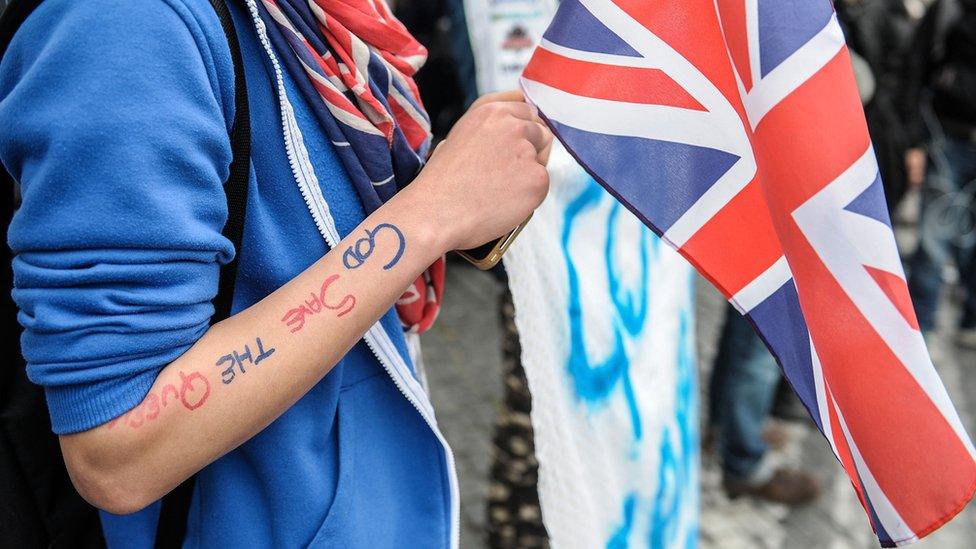 Figure wearing union jacks and holding a flag, with God Save the Queen written on their arm