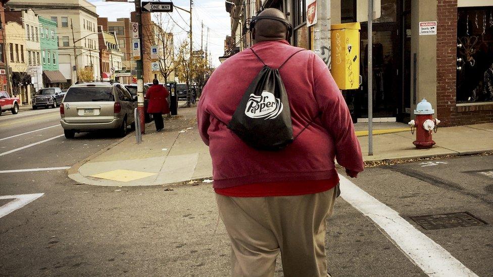 Overweight man walking across a street