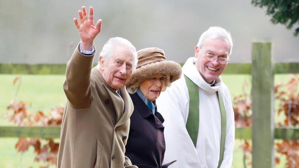 king and camilla walking with the king waving