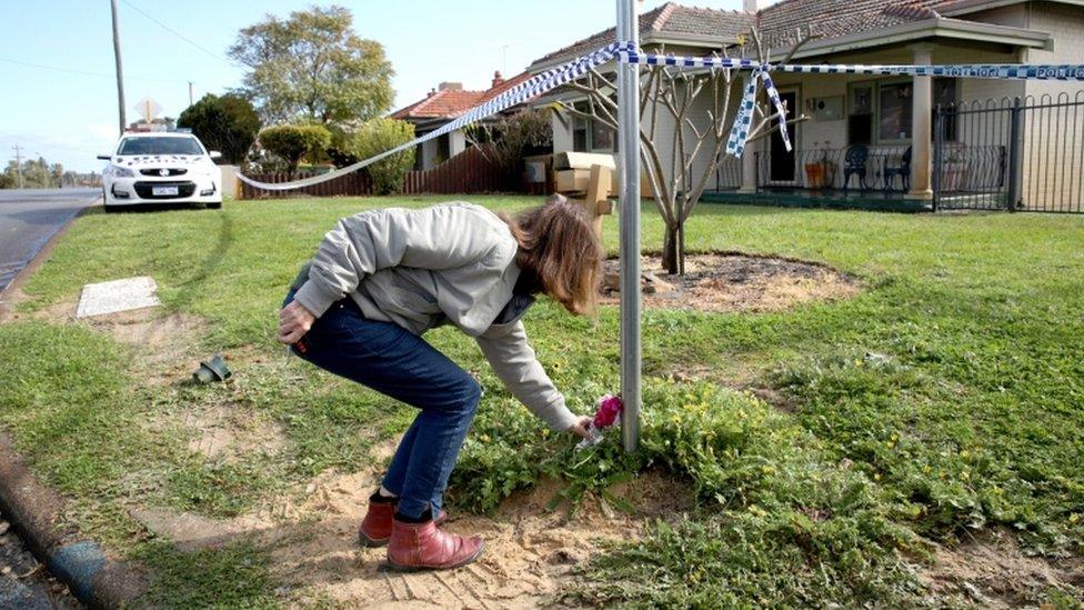 A woman lays flowers outside the home where the victims were found