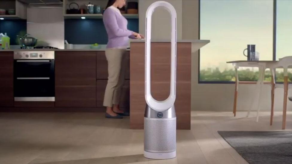 A bladeless fan stands in the centre of a kitchen , with no power cord to be seen