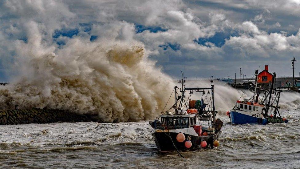 Fishing trawlers in the sea as waves crash against the harbour wall during Storm Ciaran in Folkestone, Kent