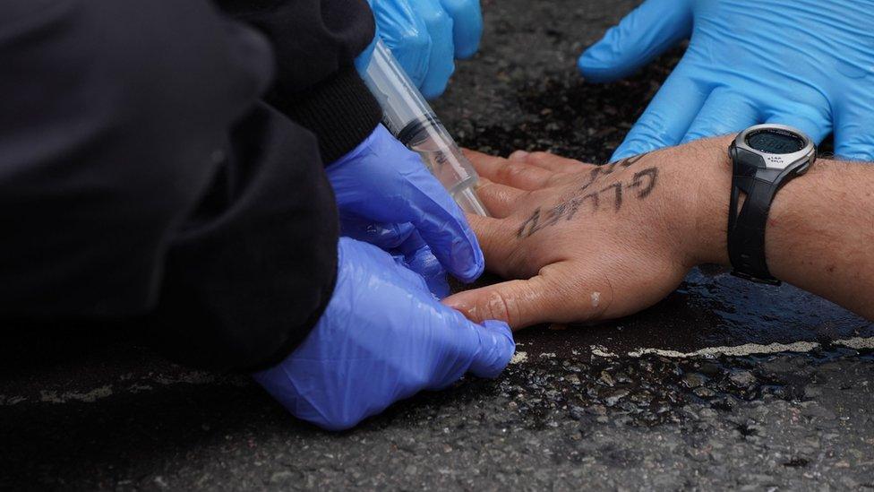 Police attempt to free a man who has glued himself to the road durin