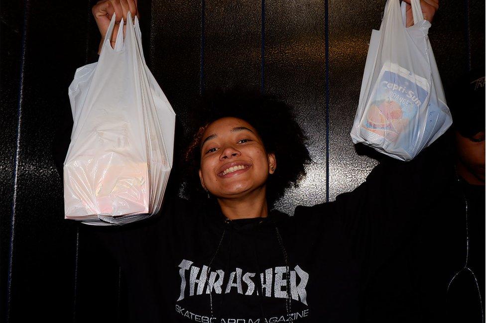 A girl holds up bags of takeaways