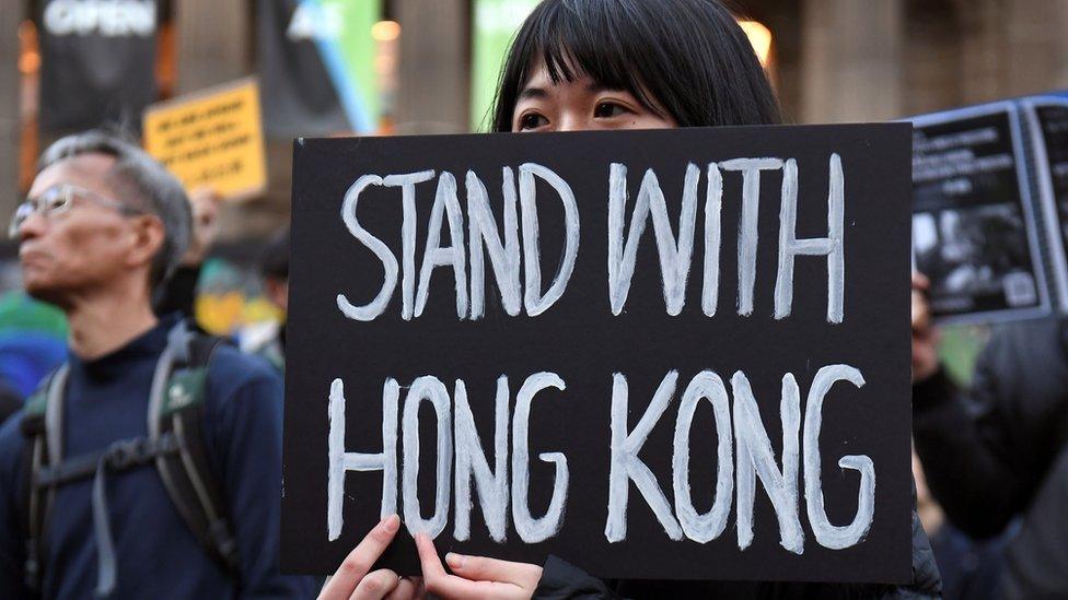 A-woman-holds-a-placard-saying-stand-with-Hong-Kong.