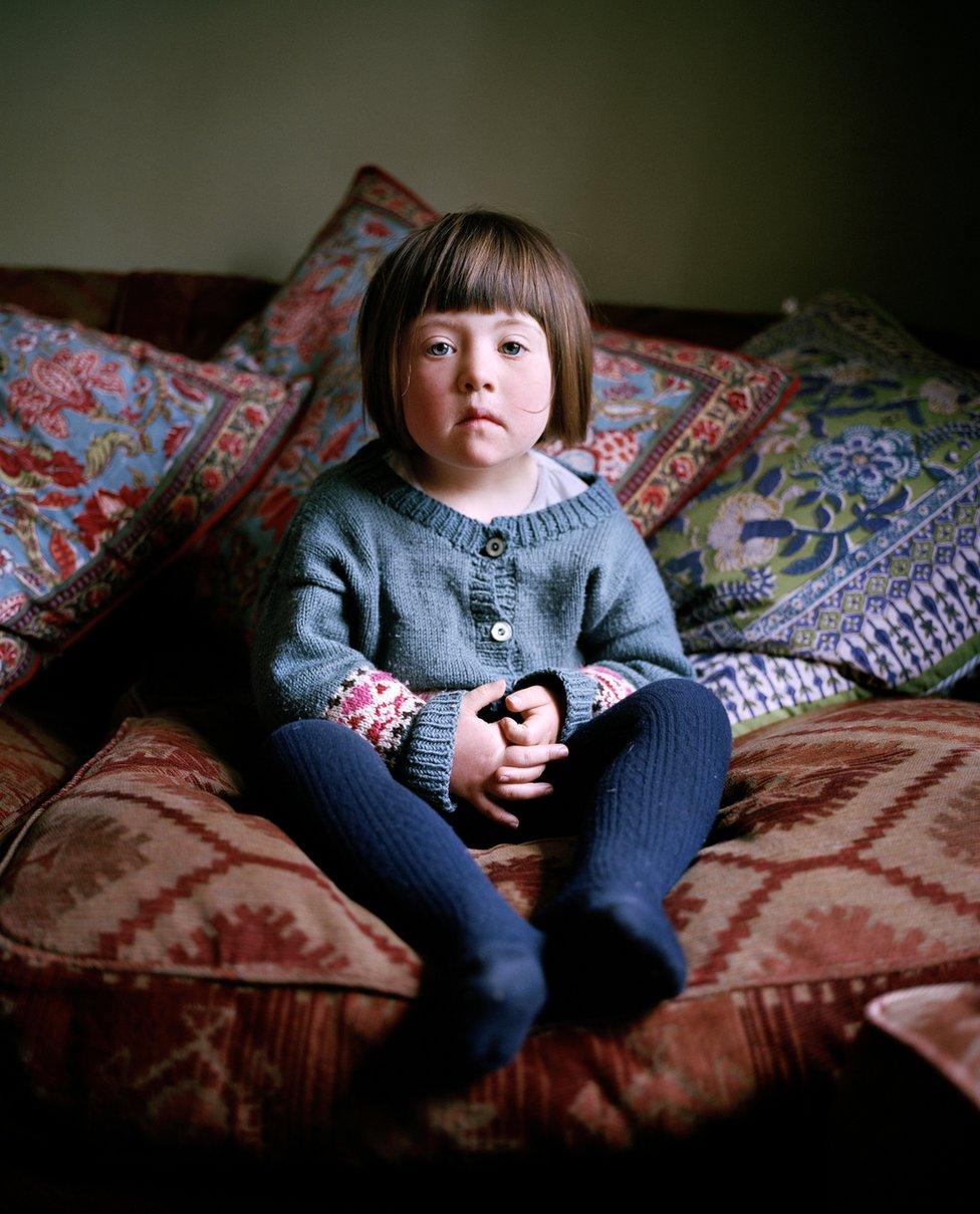 A small girl sits on the sofa and looks in to the camera