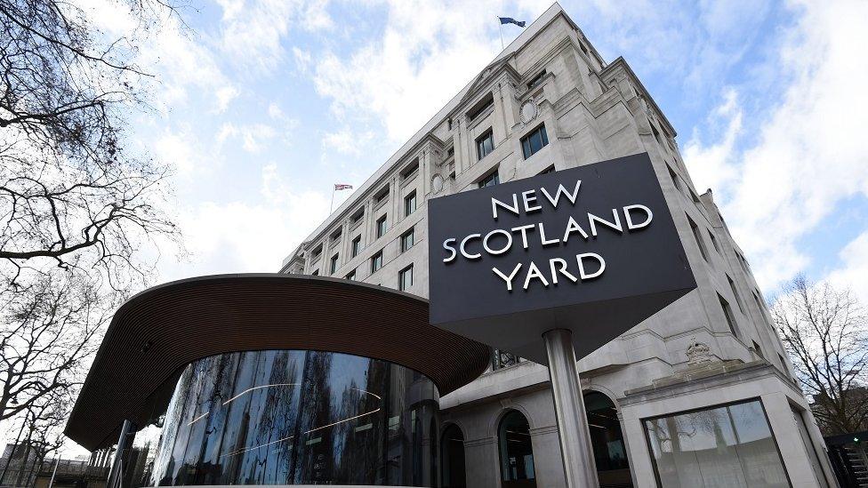 An exterior view of New Scotland Yard, with a large sign bearing the building's name in the foreground