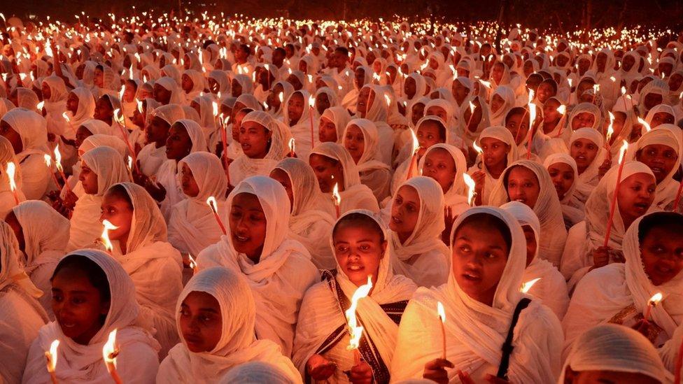 Tens of Ethiopian Orthodox Christians wearing white and holding candles during a Christmas celebration