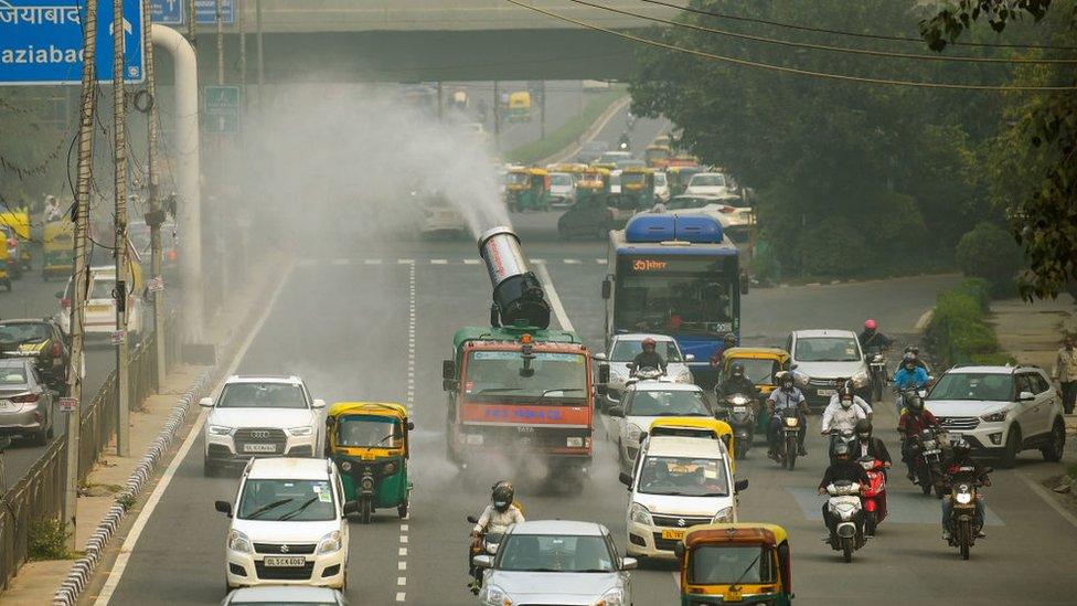 Traffic in New Delhi and a truck mounted with an anti-smog gun dispersing water.