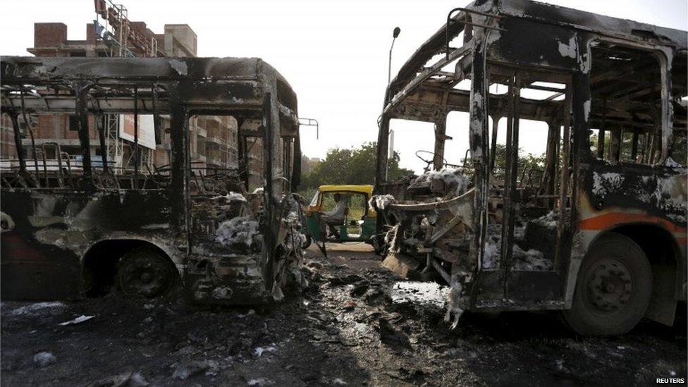 An auto rickshaw moves past damaged passenger buses which were burnt in Wednesday's clashes between protesters and police in Ahmedabad, India, August 27, 2015