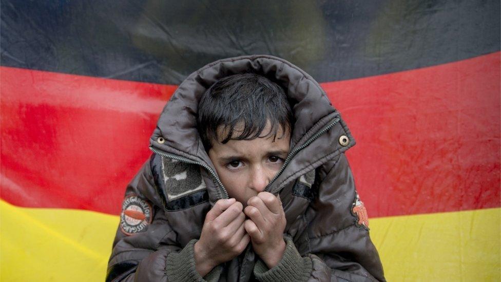 A child tries to warm his hands, backdropped by Germany's flag, as protesting migrants stage a sit-in protest on the railway tracks at northern Greek border station of Idomeni