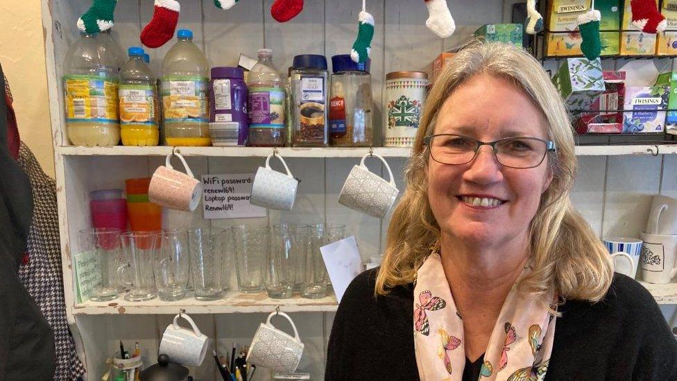 Woman with long blonde hair and glasses stands in front of bottles of squash on shelves