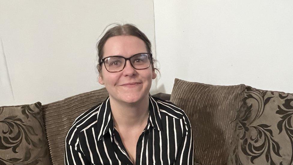 Woman in black and white top wearing glasses sits on a brown sofa