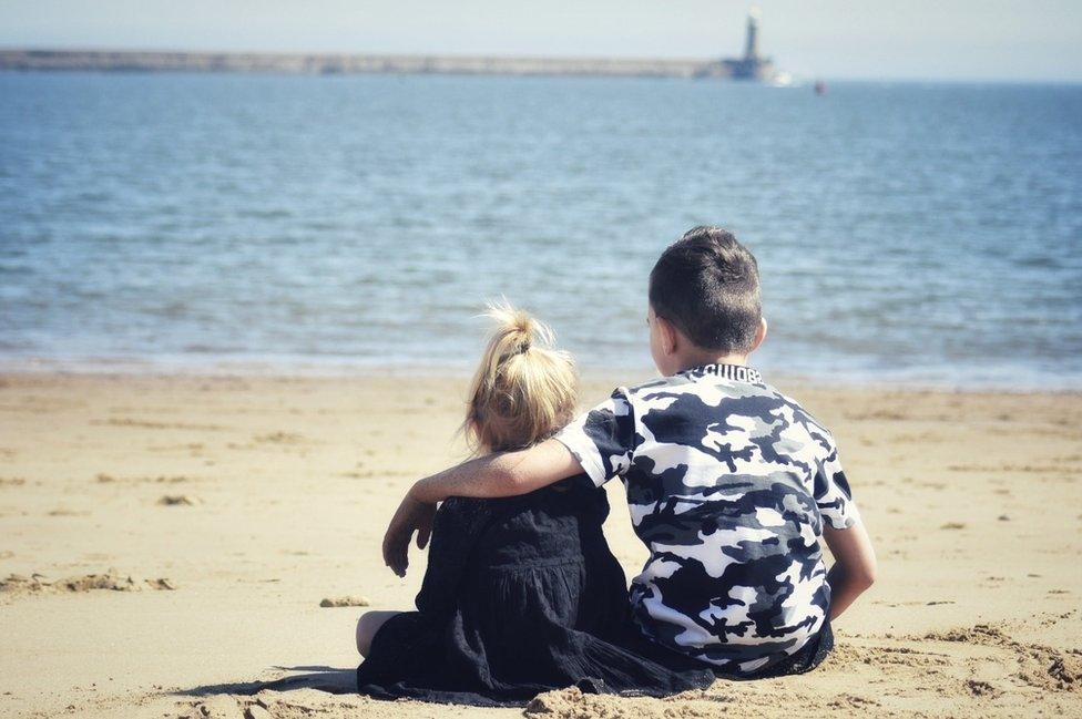 Two young children on a beach facing out to sea