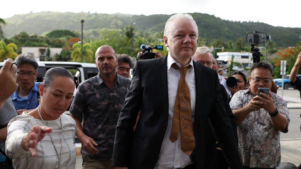 Julian Assange arrives at court in the Northern Mariana Islands surrounded by people