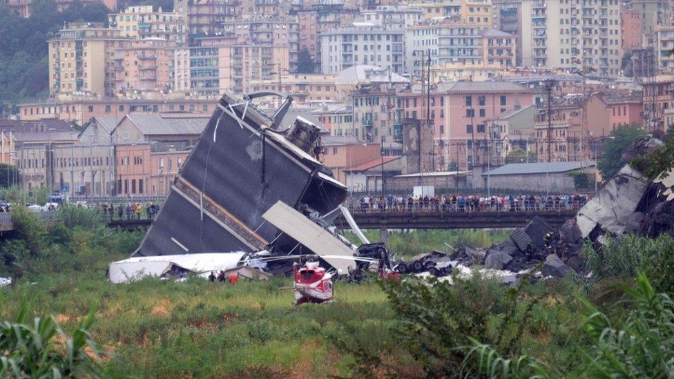 A chunk of road is pictured lying on its side as people look on at rescue efforts