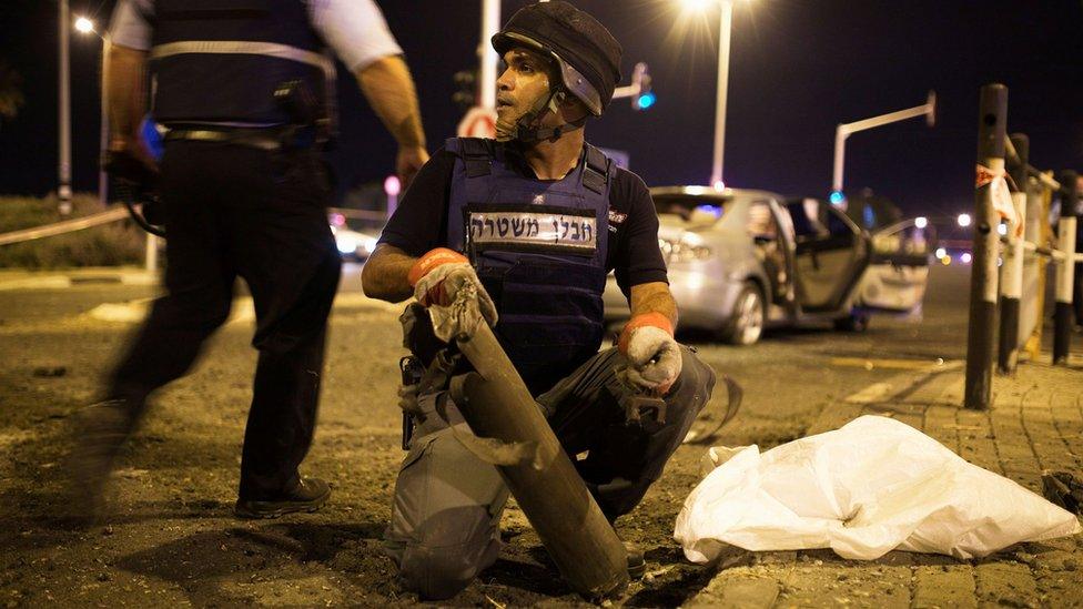 An Israeli police office removes the remains of a rocket fired from Gaza at Gan Yavne, Israel (22 August 2014)