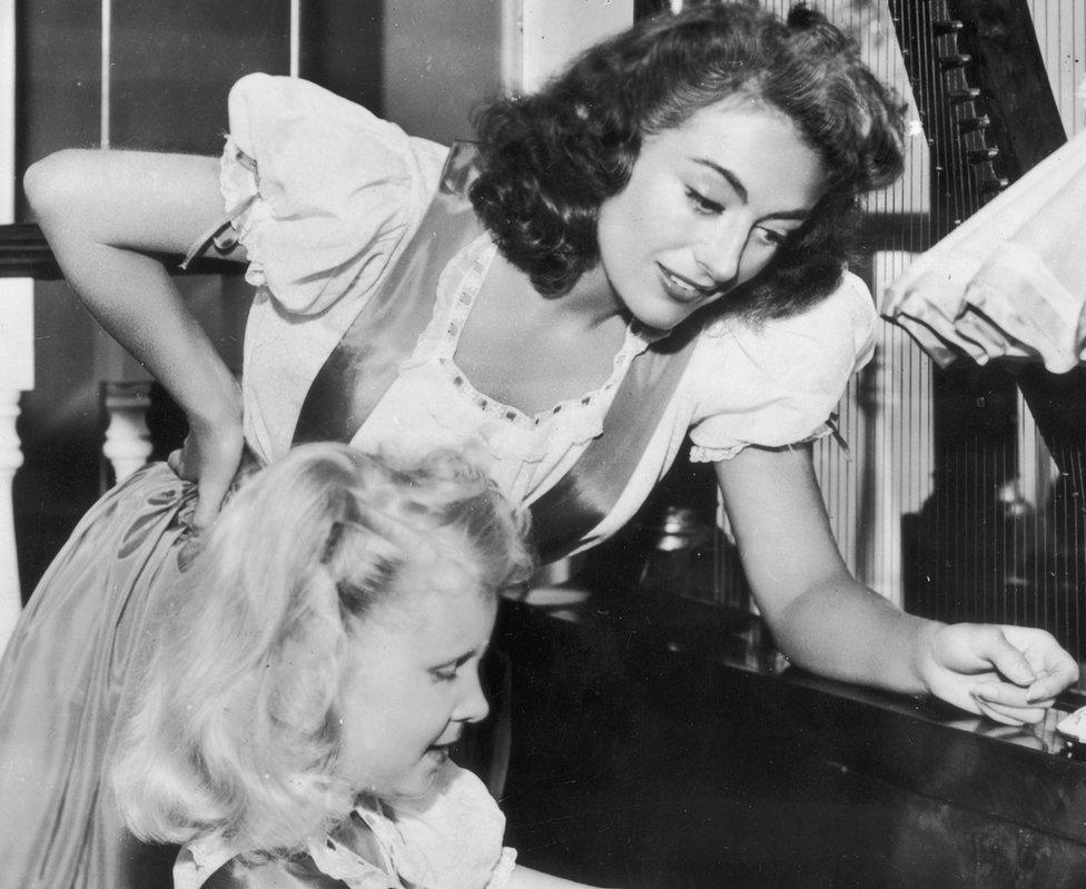 July 1947: Hollywood actress Joan Crawford (1904 - 1977) supervises her adoptive daughter Christina's piano practice.