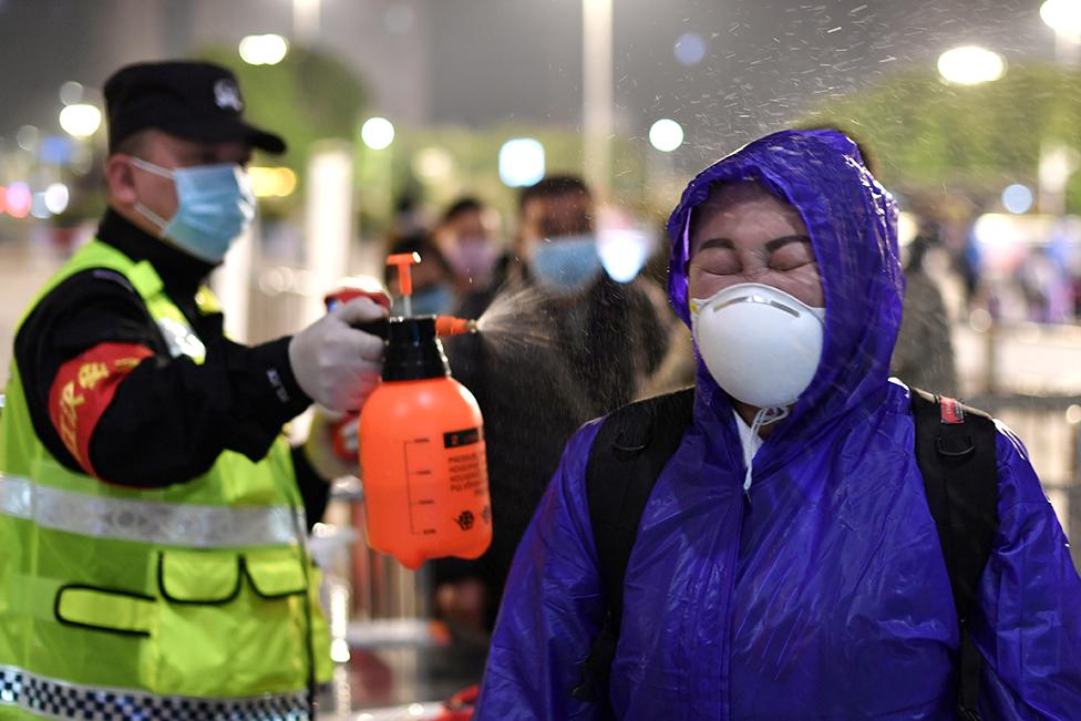 A police officer sprays disinfectant on a traveller