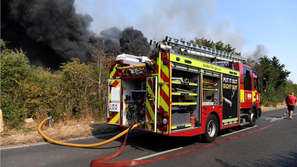 A fire truck parked near a fire that burns during a heatwave, in east London