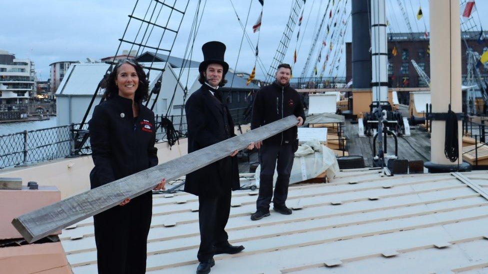 The first board was lifted during a special ceremony on Wednesday. Three people are holding up a plank of wood on board the deck of the SS Great Britain