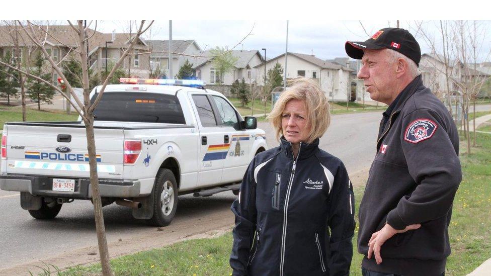 Rachel Notley and the Fort McMurray fire chief Darby Allen standing next to a police truck on an empty road