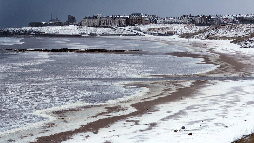 Beach covered in snow with buildings in the distance