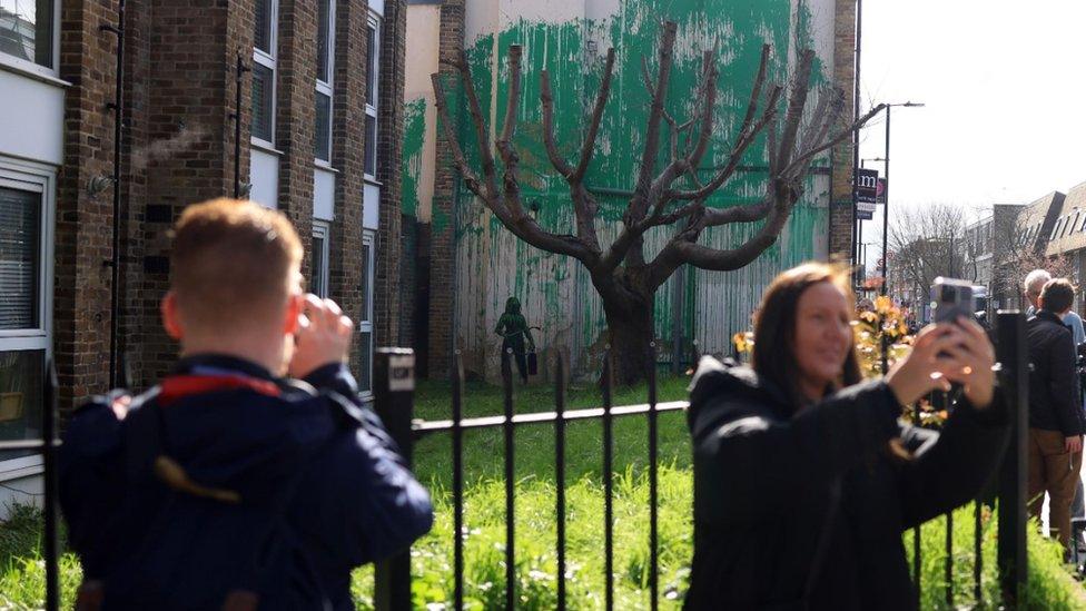 People standing in front of Banksy mural taking pictures