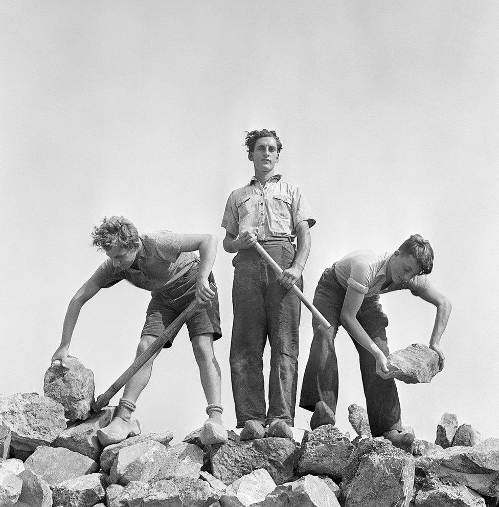 Ernst Kaufmann, centre, and unidentified Zionist youths, wearing clogs while learning construction techniques in a quarry. Werkdorp Nieuwesluis, Wieringermeer, The Netherlands, 1938-39.