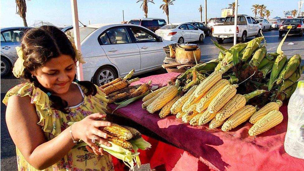 A girl carries grilled corn cobs from the stall of a pedlar on the side of a main road in Libya's capital Tripoli - 24 June 2020