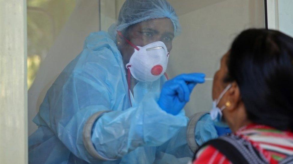 A medical worker collects a swab sample from a woman in India