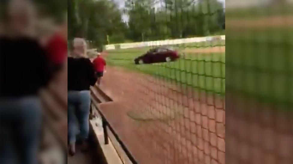 Bystanders watch car on baseball field